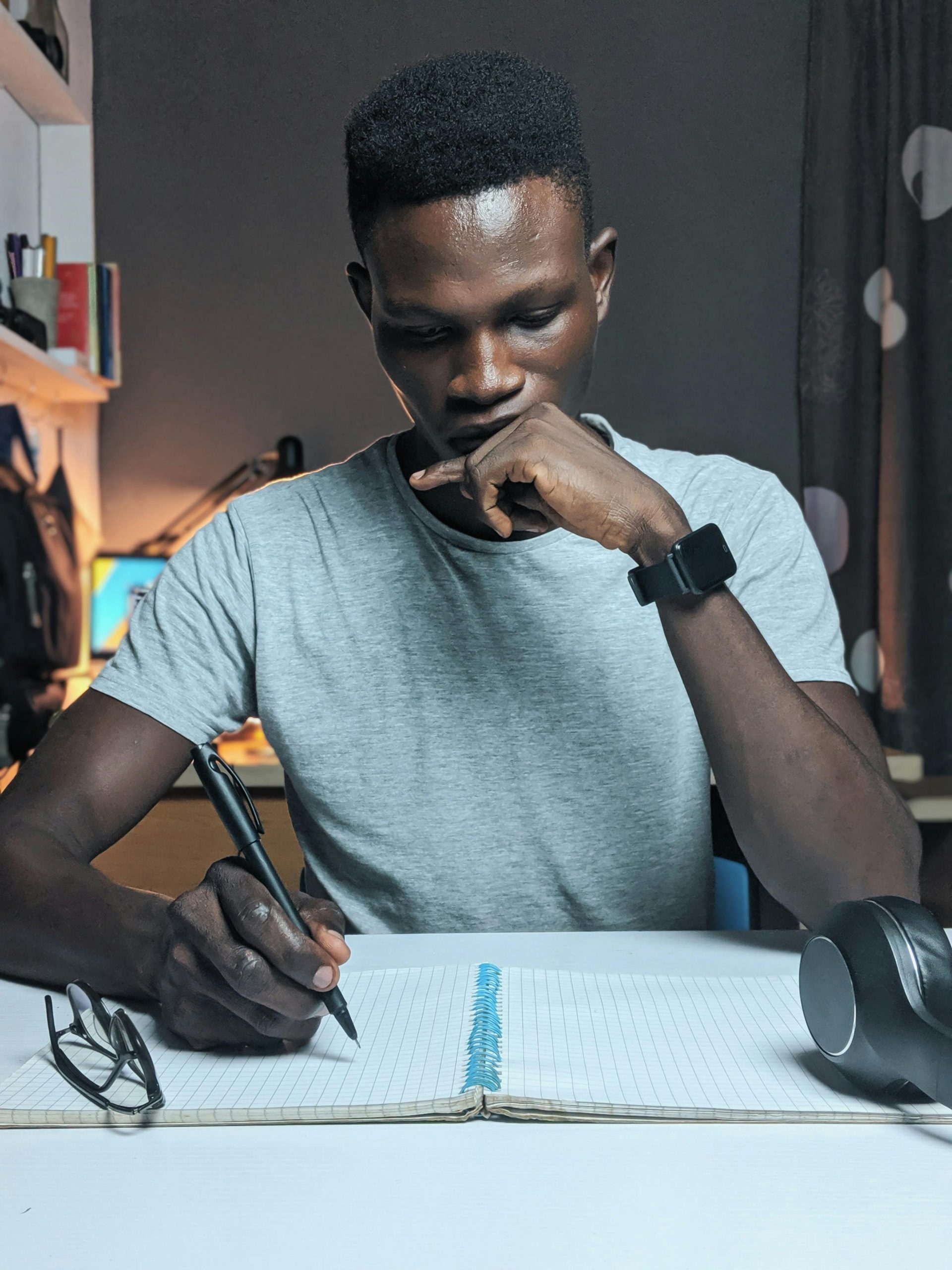 Man deeply focused while writing in a notebook on a desk with a thoughtful expression.