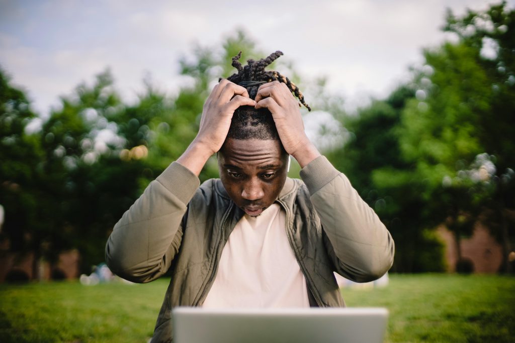 pexels-photo-4560092-4560092 Upset young African American male freelancer clutching head with hands after failure in project while working remotely in park
