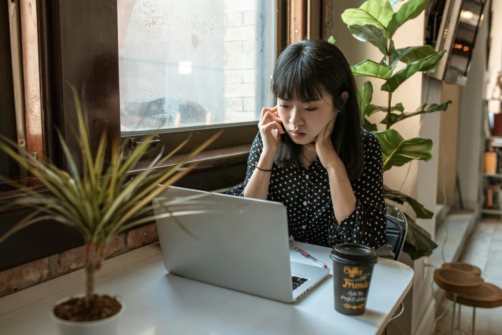 Asian woman focused on work in a modern office setting with laptop and coffee.