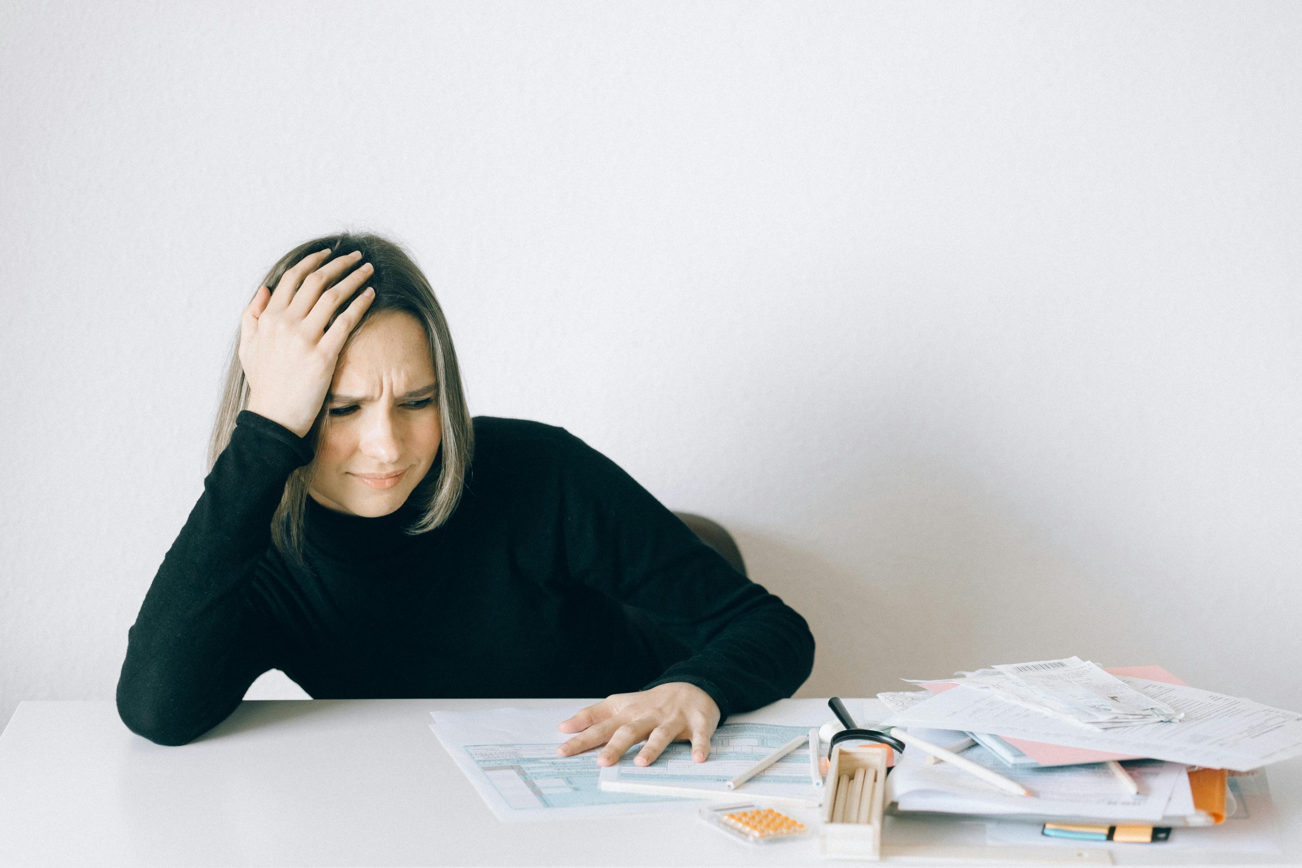 Woman in black sweater stressed with financial paperwork, overwhelmed at white table.