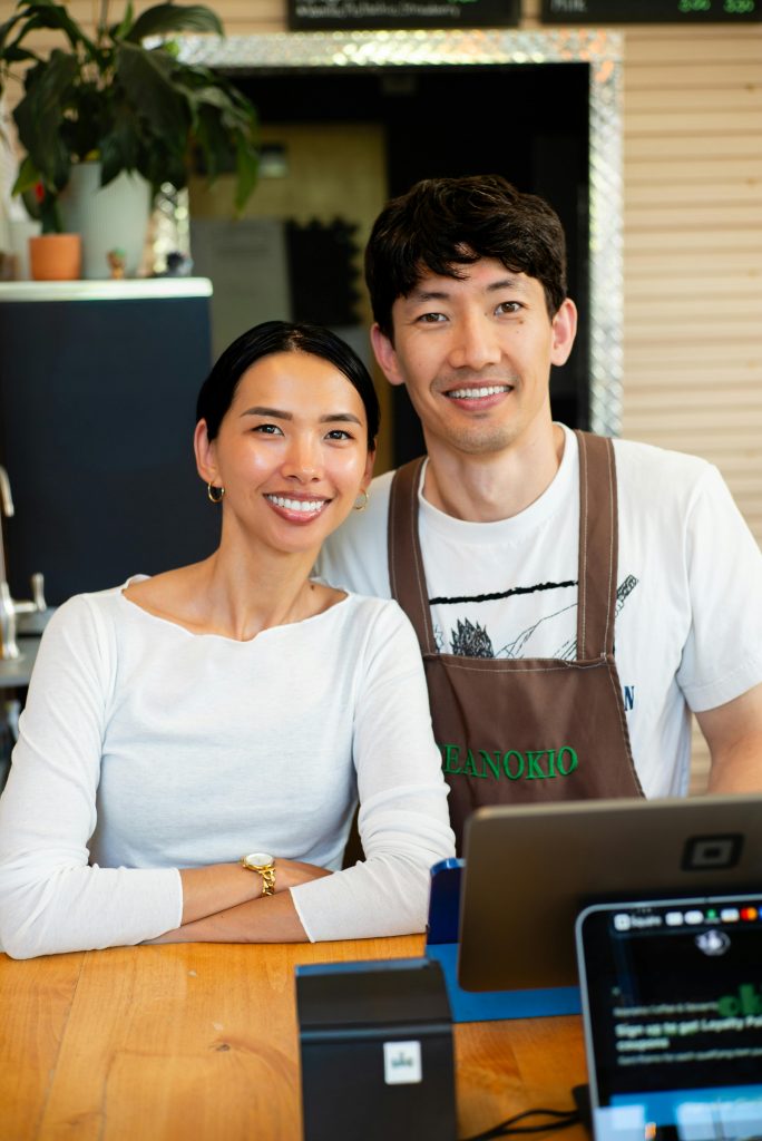 pexels-photo-34164499-34164499 Portrait of two smiling coffee shop owners standing behind counter. Ideal for business and small enterprise themes.
